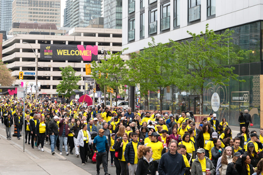 An outdoor photo of participants and donors in the We Walk UHNITED event. It’s a large crowd with thousands of people walking in the street with yellow t-shirts and event signs.